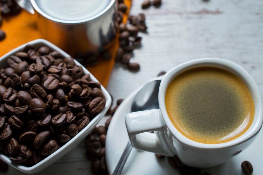 coffee beans next to a cup of freshly brewed black coffee in a white mug