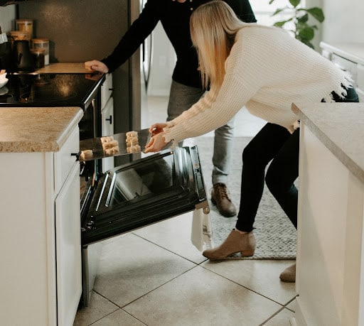 husband wife placing cookies in the oven